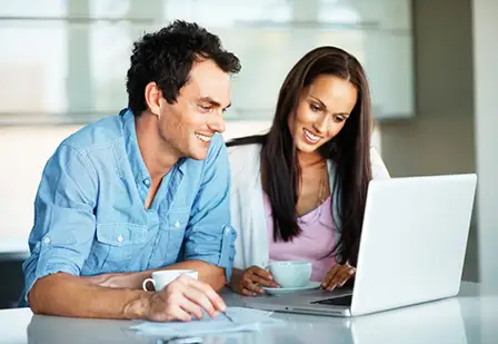 Happy couple using laptop while drinking coffee.