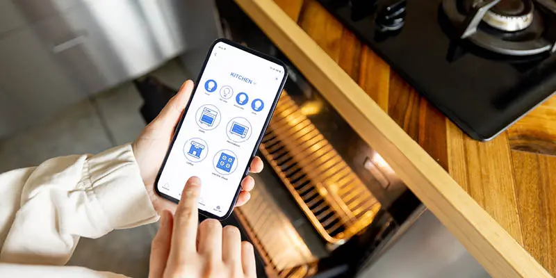Hand holding smartphone controlling kitchen devices via app