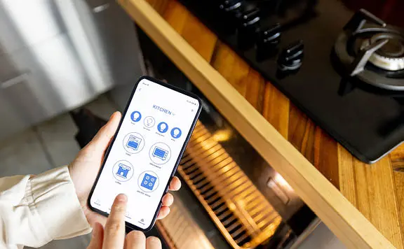 Hand holding smartphone controlling kitchen devices via app