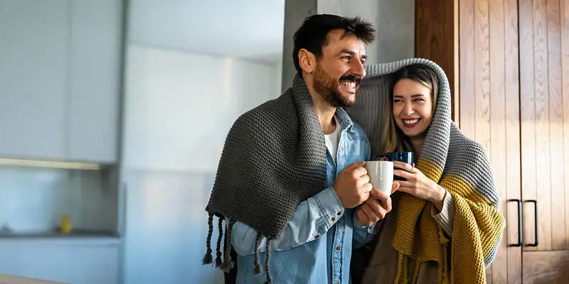 Happy couple sharing blanket enjoying morning coffee