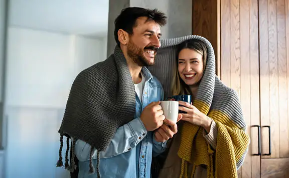 Happy couple sharing blanket enjoying morning coffee
