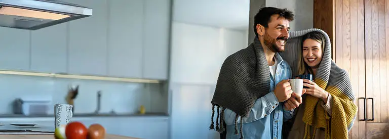 Happy couple sharing blanket enjoying morning coffee