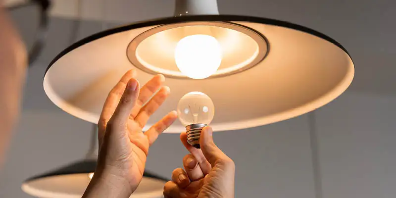 Person changing incandescent bulb to LED in pendant light