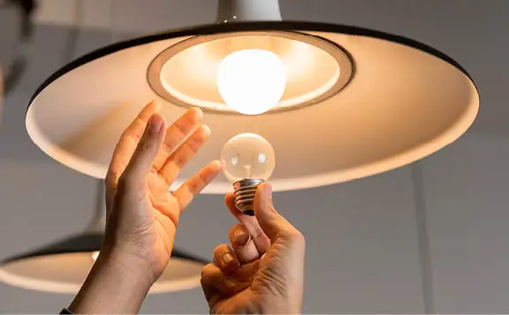 Person changing incandescent bulb to LED in pendant light