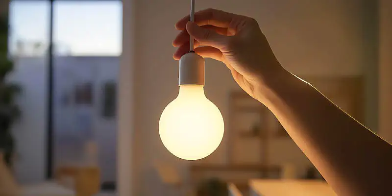 Person holding cord of illuminated pendant light bulb