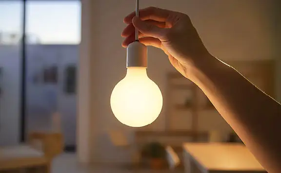 Person holding cord of illuminated pendant light bulb