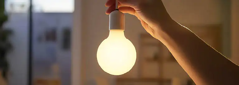 Person holding cord of illuminated pendant light bulb