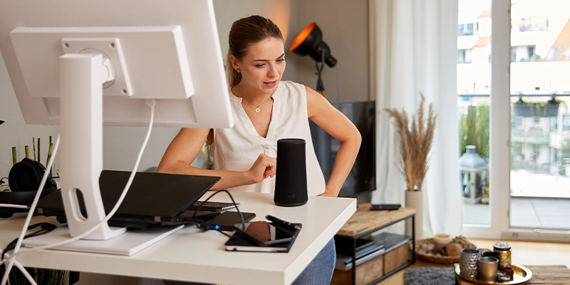 Woman at home desk talking to smart home speaker device