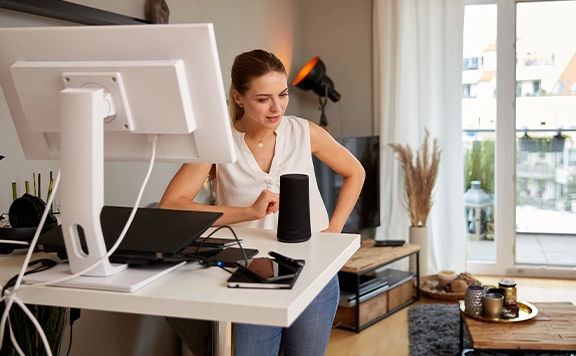 Woman at home desk talking to smart home speaker device