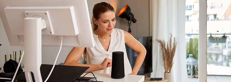 Woman at home desk talking to smart home speaker device