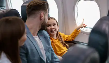 Family sitting next to airplane window and a little kid pointing to something outside the window