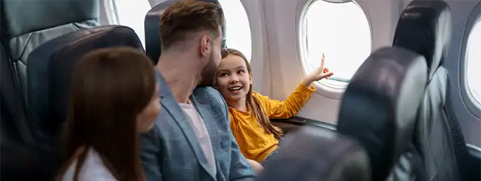 Family sitting next to airplane window and a little kid pointing to something outside the window
