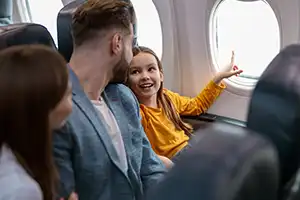 Family sitting next to airplane window and a little kid pointing to something outside the window