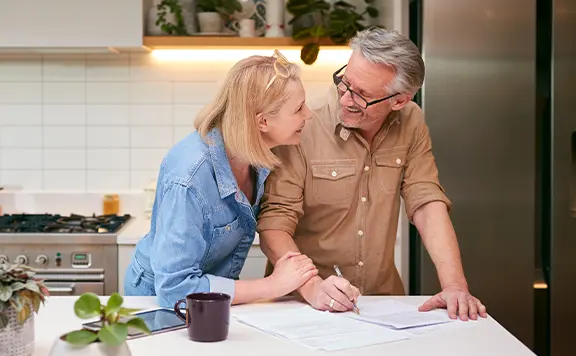 older-couple-standing-at-kitchen-island-looking-at-bills
