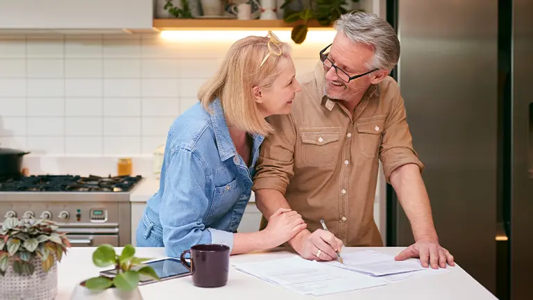older-couple-standing-at-kitchen-island-looking-at-bills