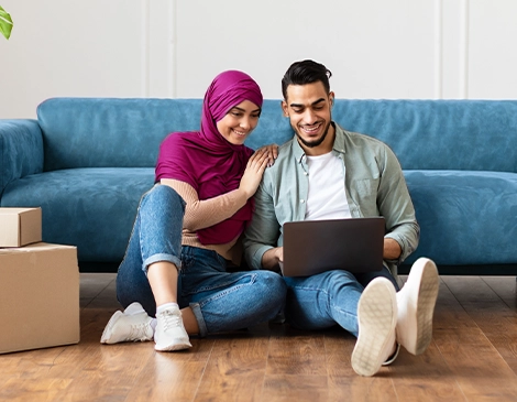 Loving couple sitting on the floor in the middle of a move while searching for something on a laptop