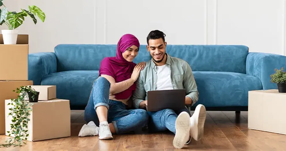 Couple sitting on the floor while unpacking and looking at their laptop